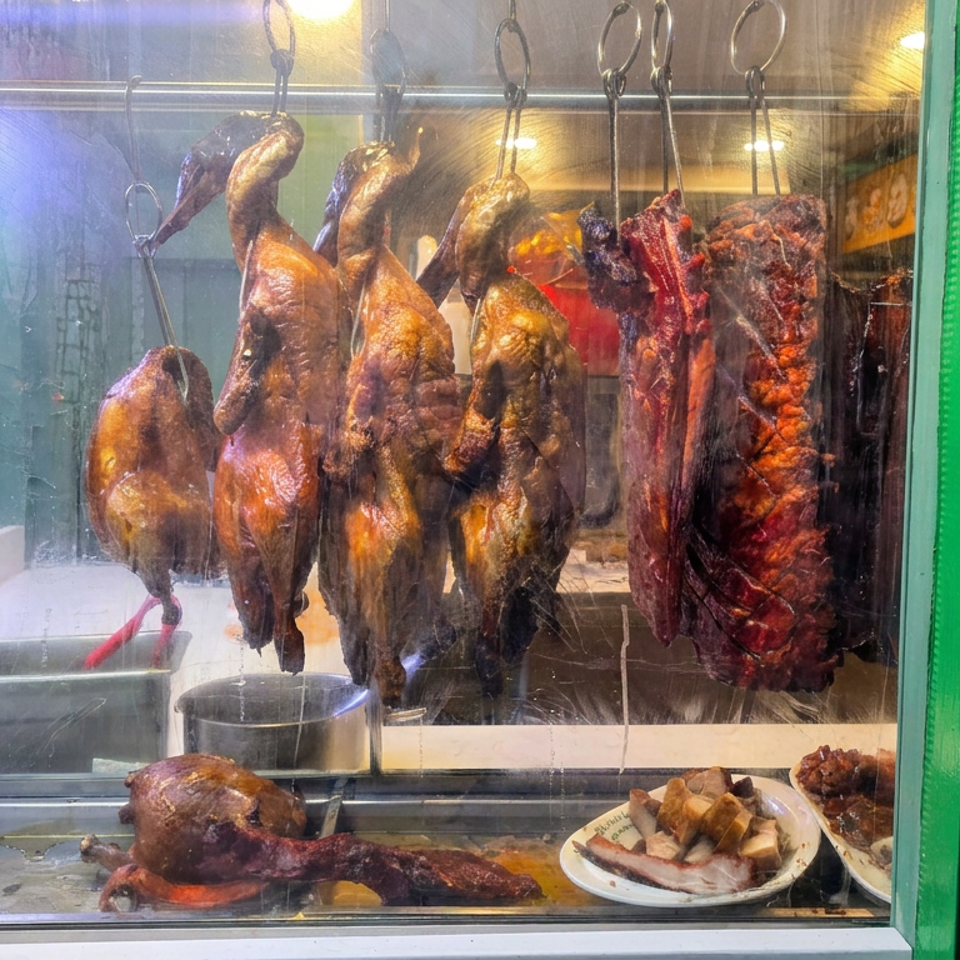 Roasted ducks and assorted meats hang in a restaurant display case beside plates of sliced pork and cooked dishes.